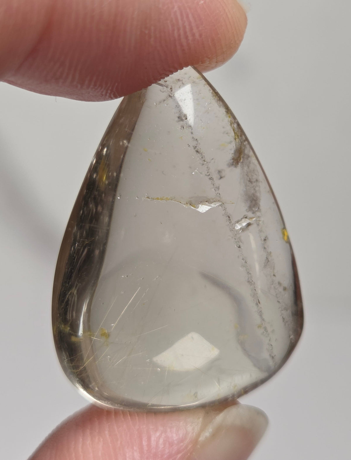 Clear quartz teardrrop shaped crystal with gold rutile inclusions held between fingers