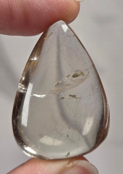 Clear quartz teardrrop shaped crystal with gold rutile inclusions held between fingers