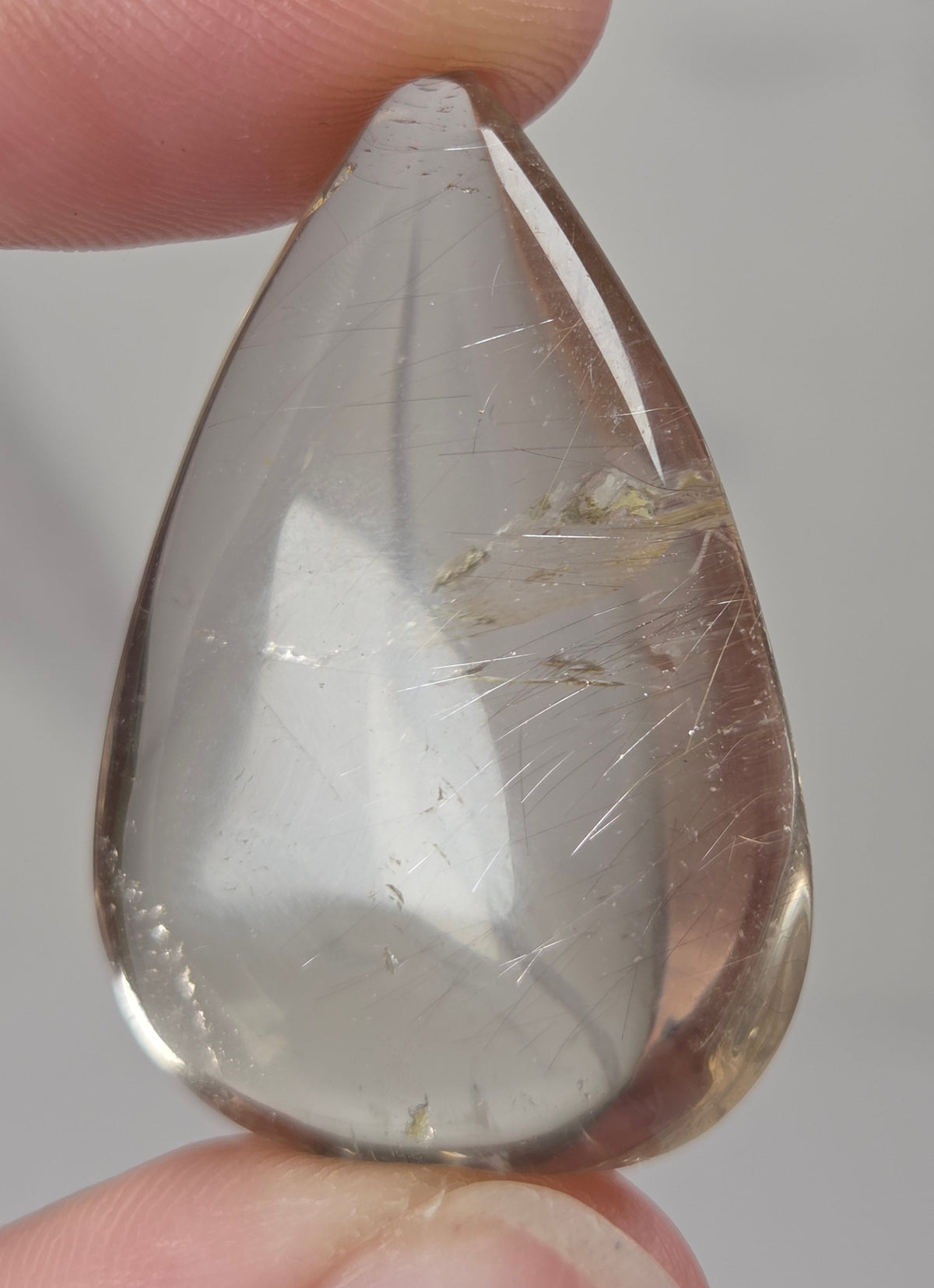 Clear quartz teardrrop shaped crystal with gold rutile inclusions held between fingers