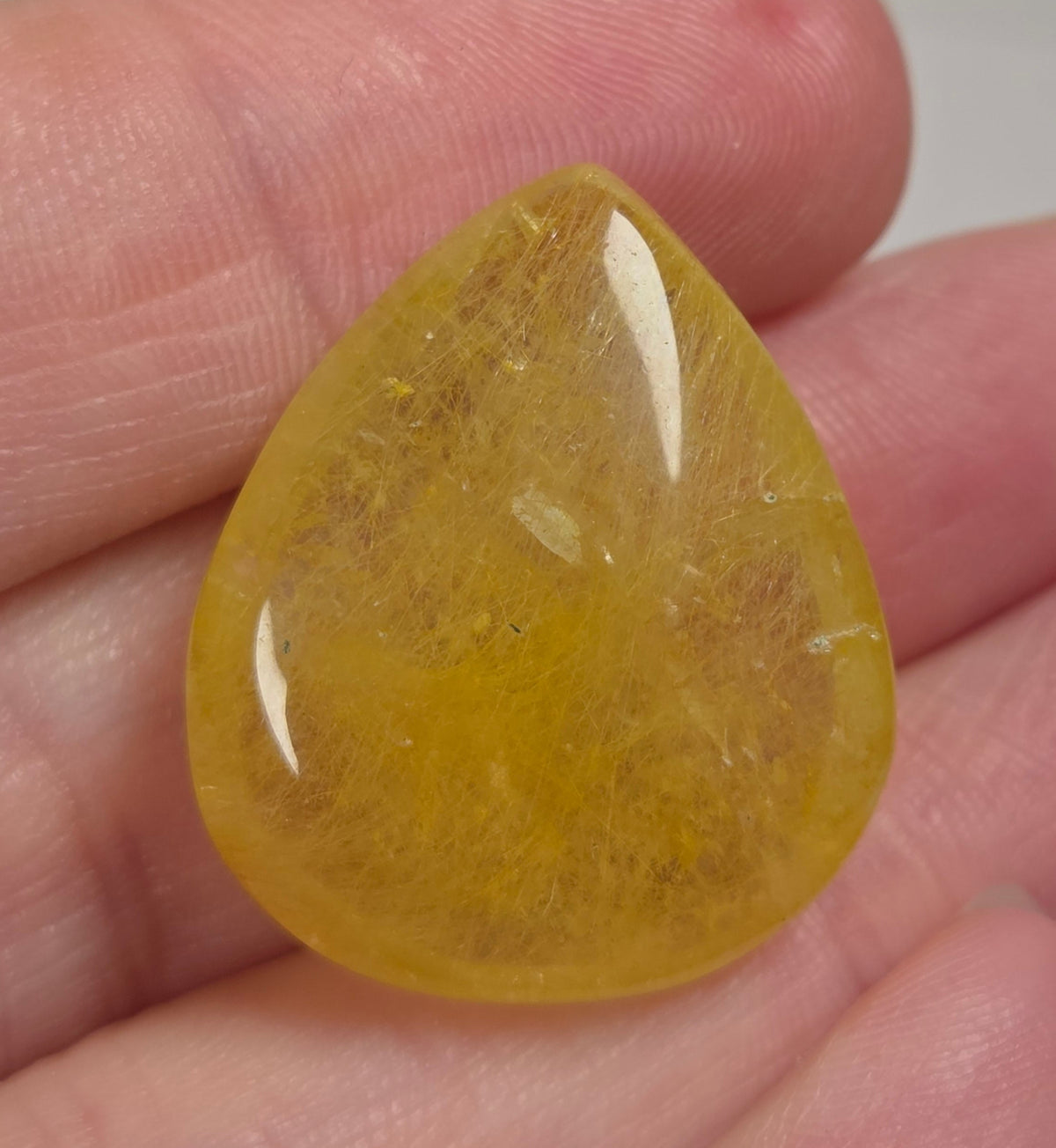 Clear quartz teardrrop shaped crystal with gold rutile inclusions held between fingers