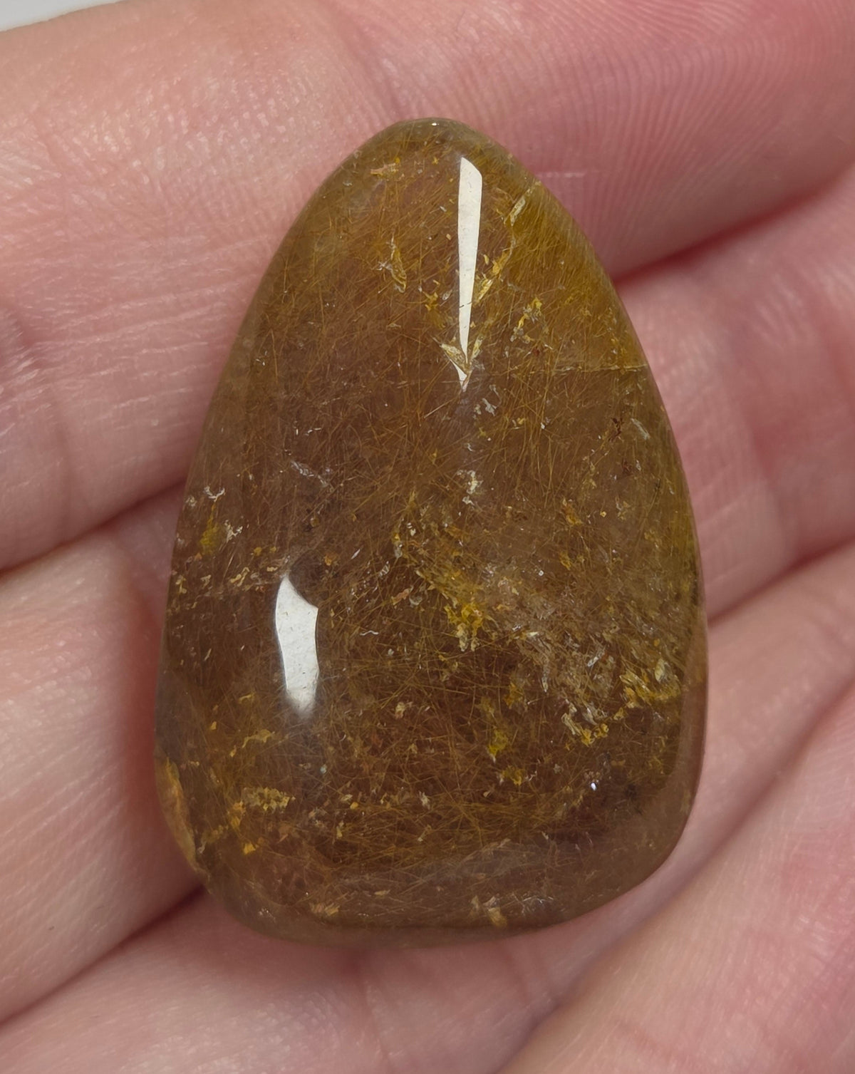 Clear quartz teardrrop shaped crystal with gold rutile inclusions held between fingers