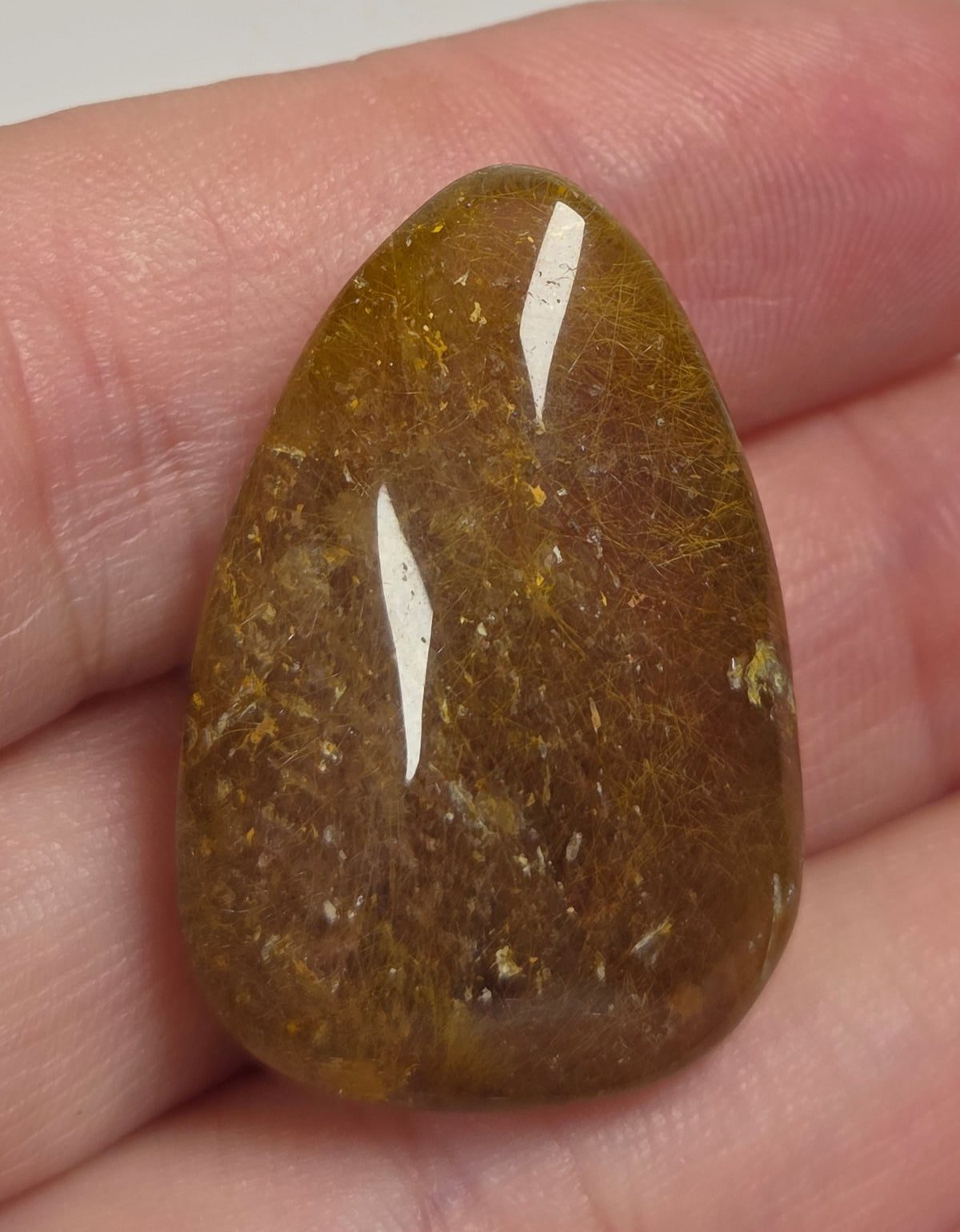 Clear quartz teardrrop shaped crystal with gold rutile inclusions held between fingers