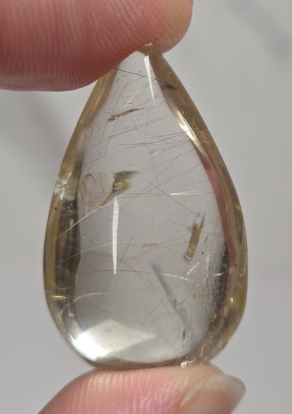 Clear quartz teardrrop shaped crystal with gold rutile inclusions held between fingers