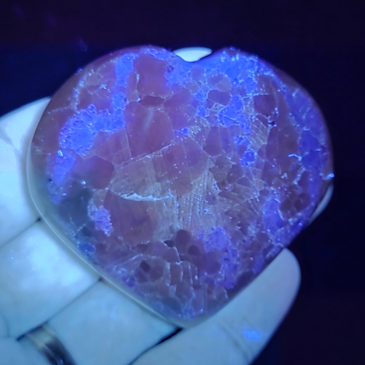 Hand holding a white crystal heart with purple coloring under UV light against a black background