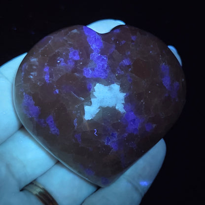 Hand holding a white crystal heart with purple coloring under UV light against a black background