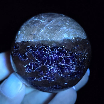 Crystal sphere carving under UV light  being held by a hand against a black background