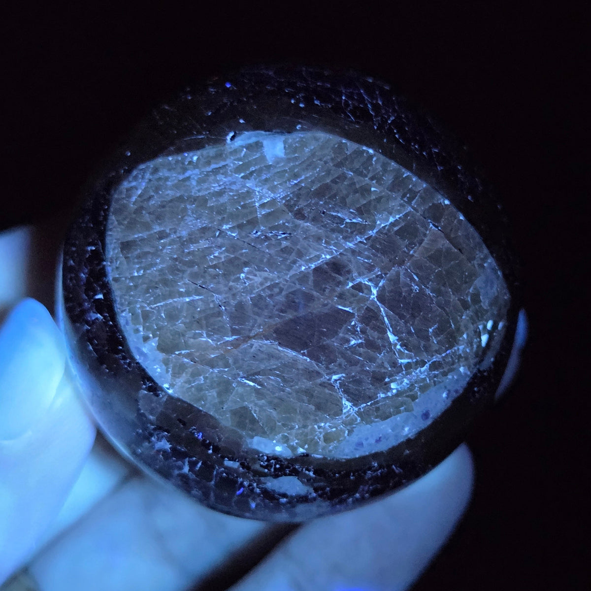 Crystal sphere carving under UV light  being held by a hand against a black background