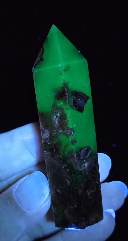 Volcano Agate polished point being held in a hand showing green  color under UV lighting against a  black background