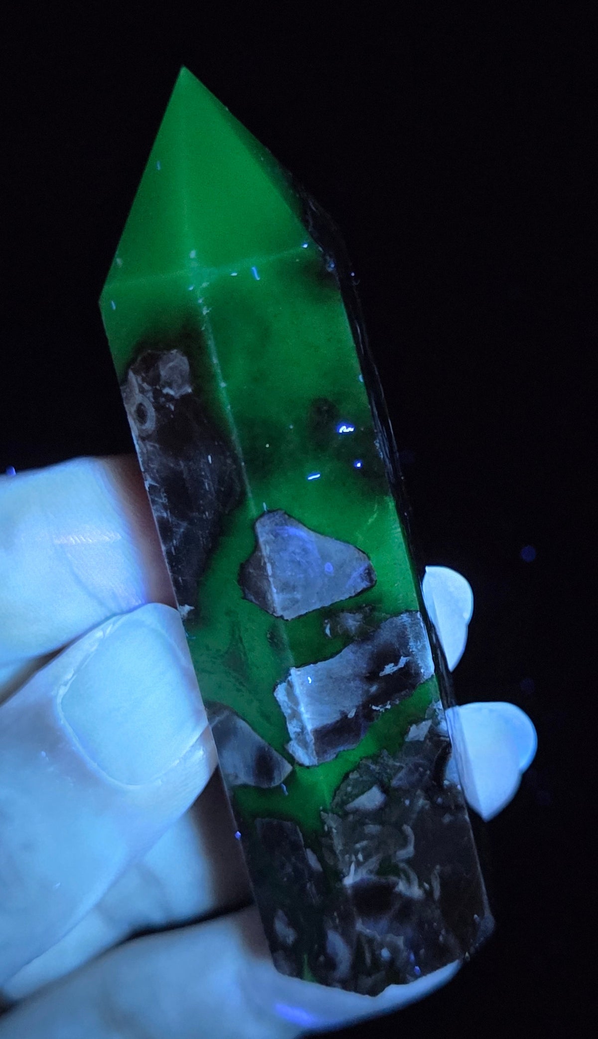 Volcano Agate polished point being held in a hand showing green  color under UV lighting against a  black background