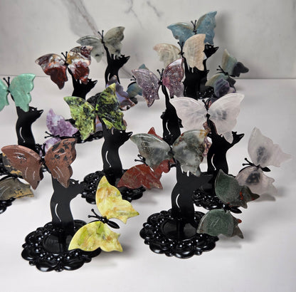 A group of decorative butterfly-shaped crystal holders on black stands, arranged on a white surface against a light gray marble-patterned background.
