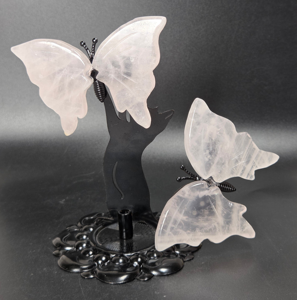 Two translucent white butterfly sculptures mounted on a black decorative stand against a dark gray studio background.