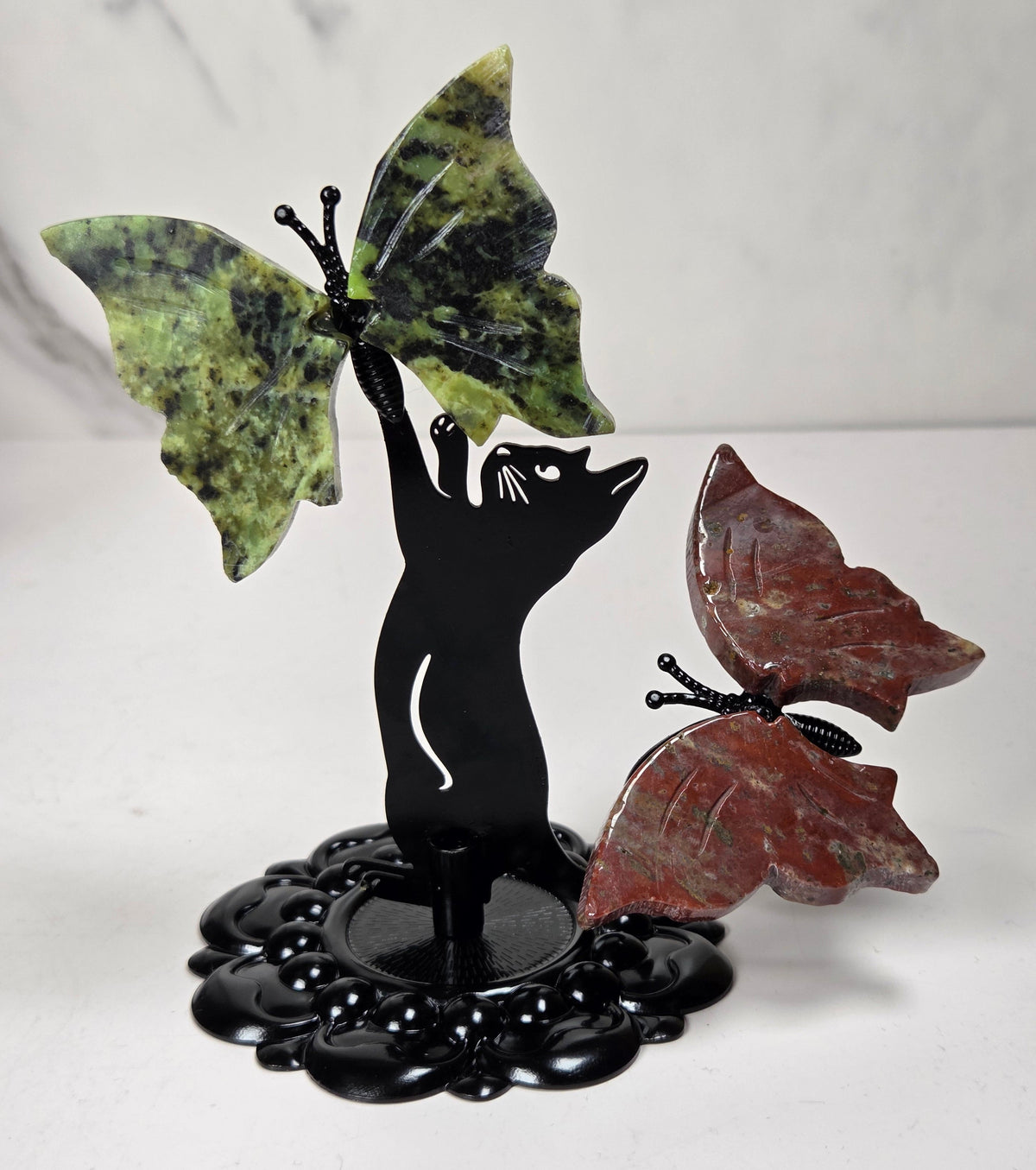 A decorative butterfly sculpture featuring a black silhouette cat on a glossy black base, with one green marbled butterfly wing and one reddish-brown marbled butterfly wing.