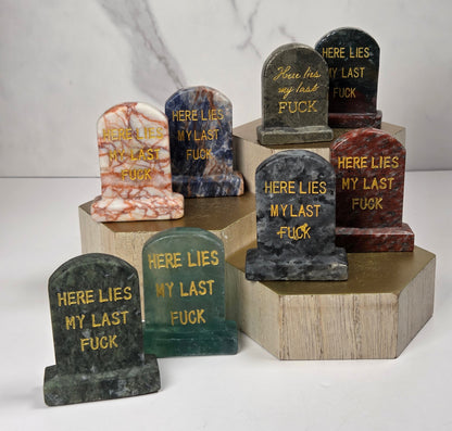 Collection of various colored crystal tombstone carvings with gold lettering on a wooden stand against a white background