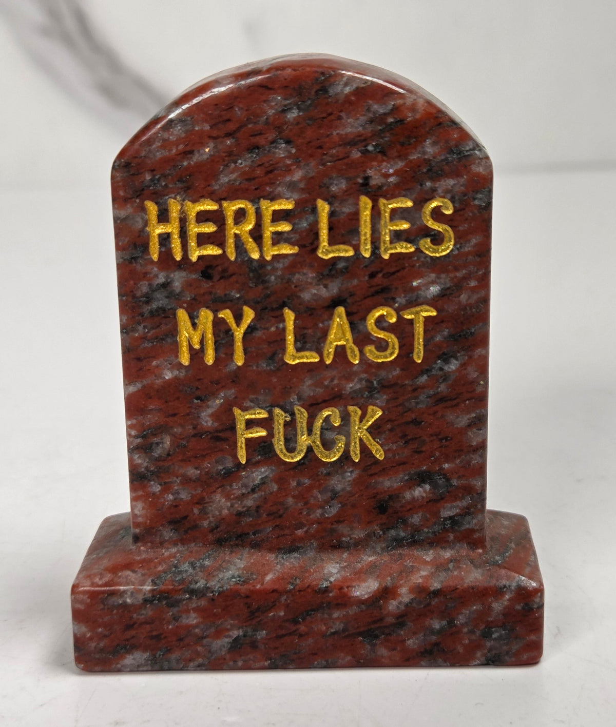 Red and black crystal tombstone carving with gold lettering against a white background