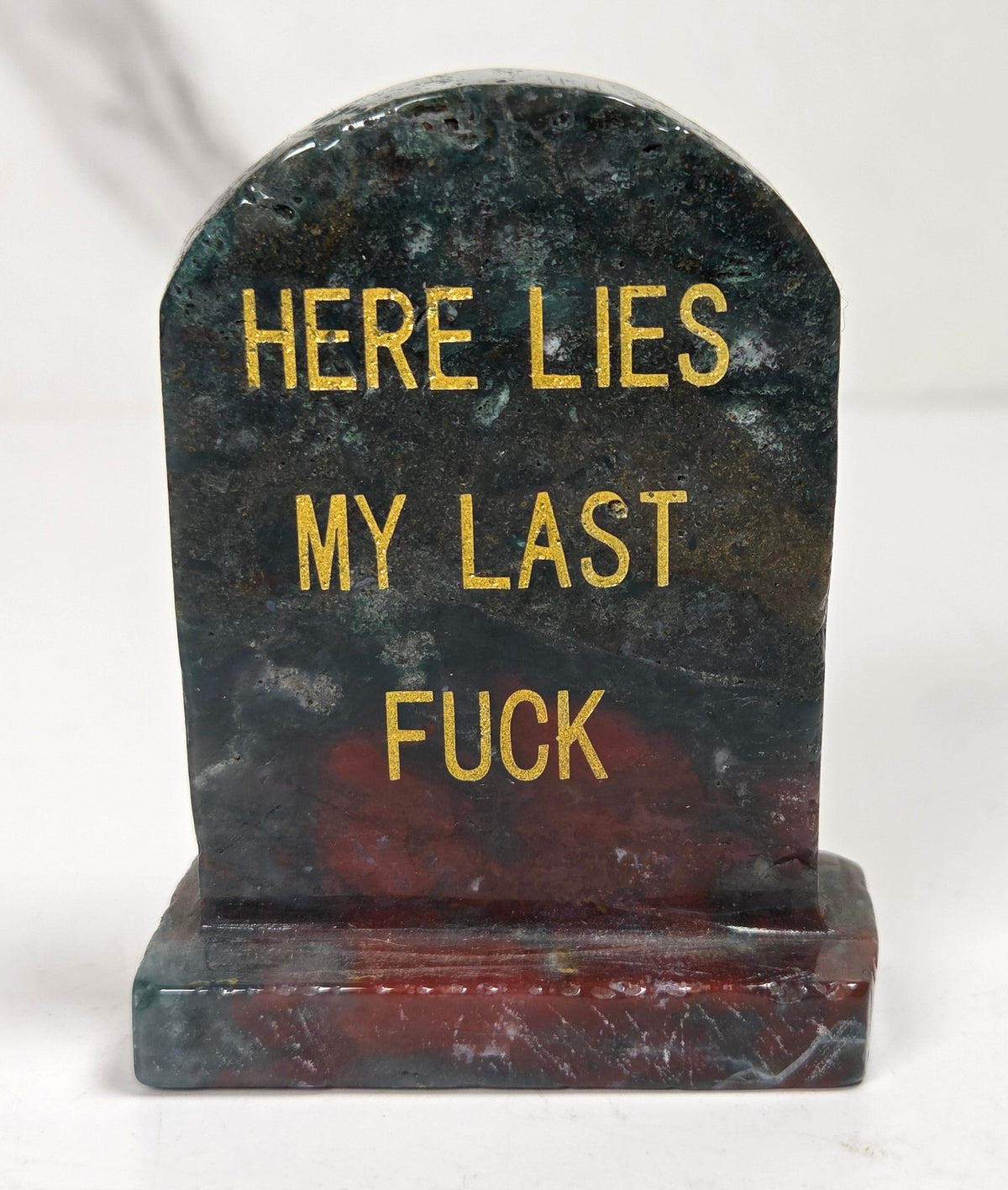 Green and red crystal tombstone carving with gold lettering against a white background