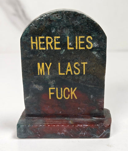 Green and red crystal tombstone carving with gold lettering against a white background