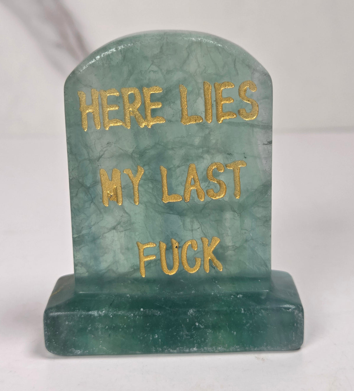 Translucent green crystal tombstone carving with gold lettering against a white background