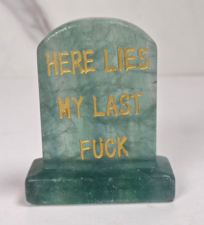 Translucent green crystal tombstone carving with gold lettering against a white background