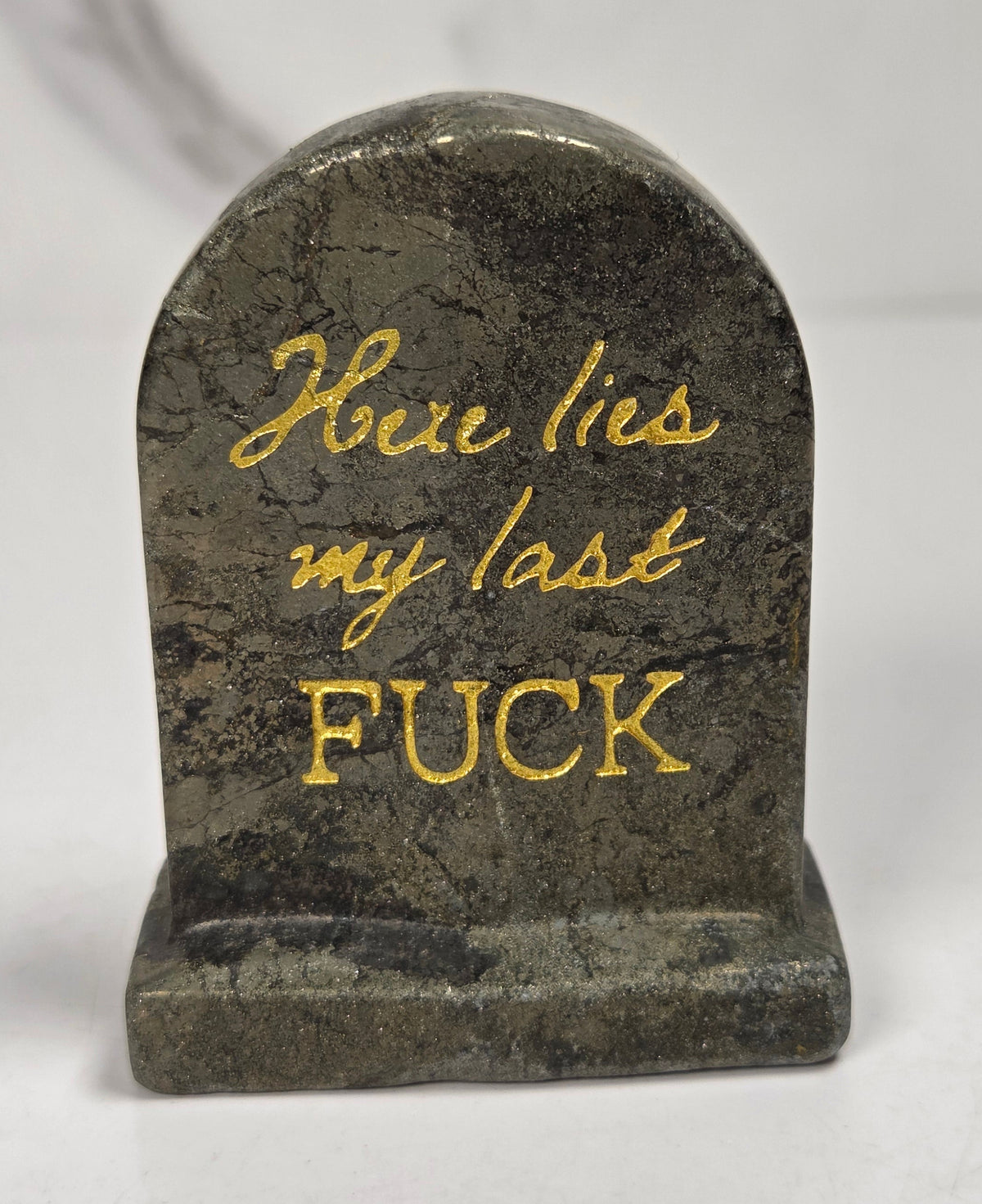 Golden pyrite crystal tombstone carving with gold lettering against a white background