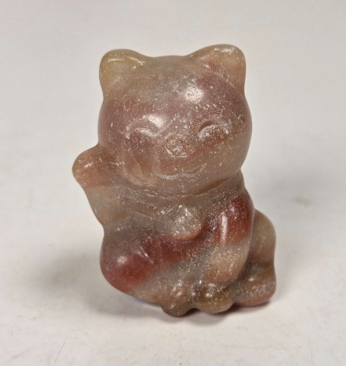 Pink banded crystal cat carving on a light gray background