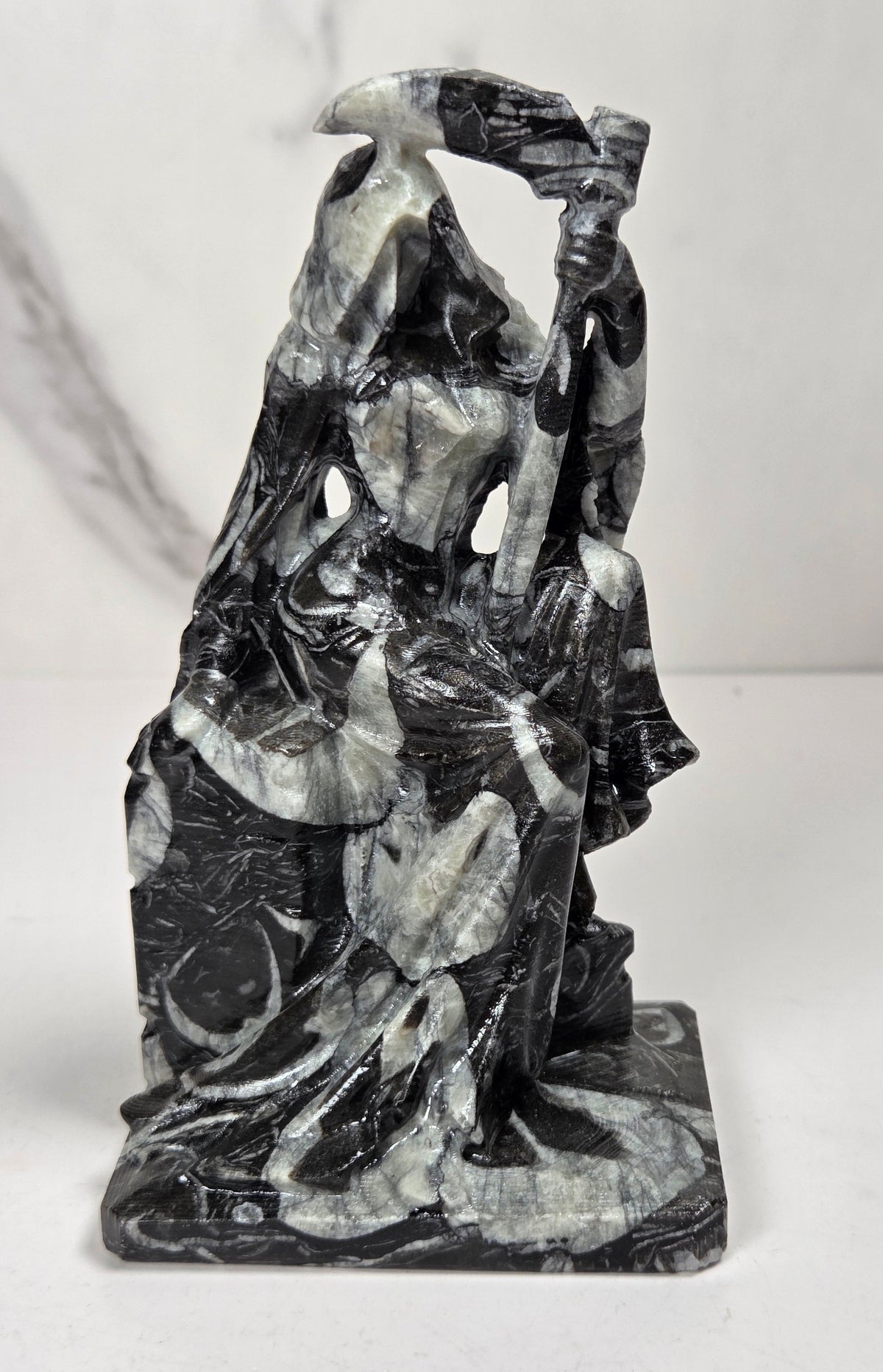 faceless lady reaper carving made of a  marbled black and white mineral against a marbled white background