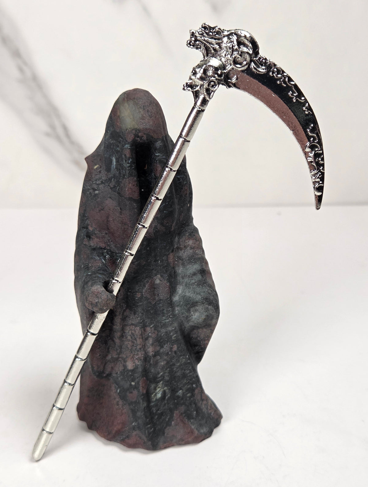 Reaper style crystal carving with black and red coloring with a metal scythe against a marbled background