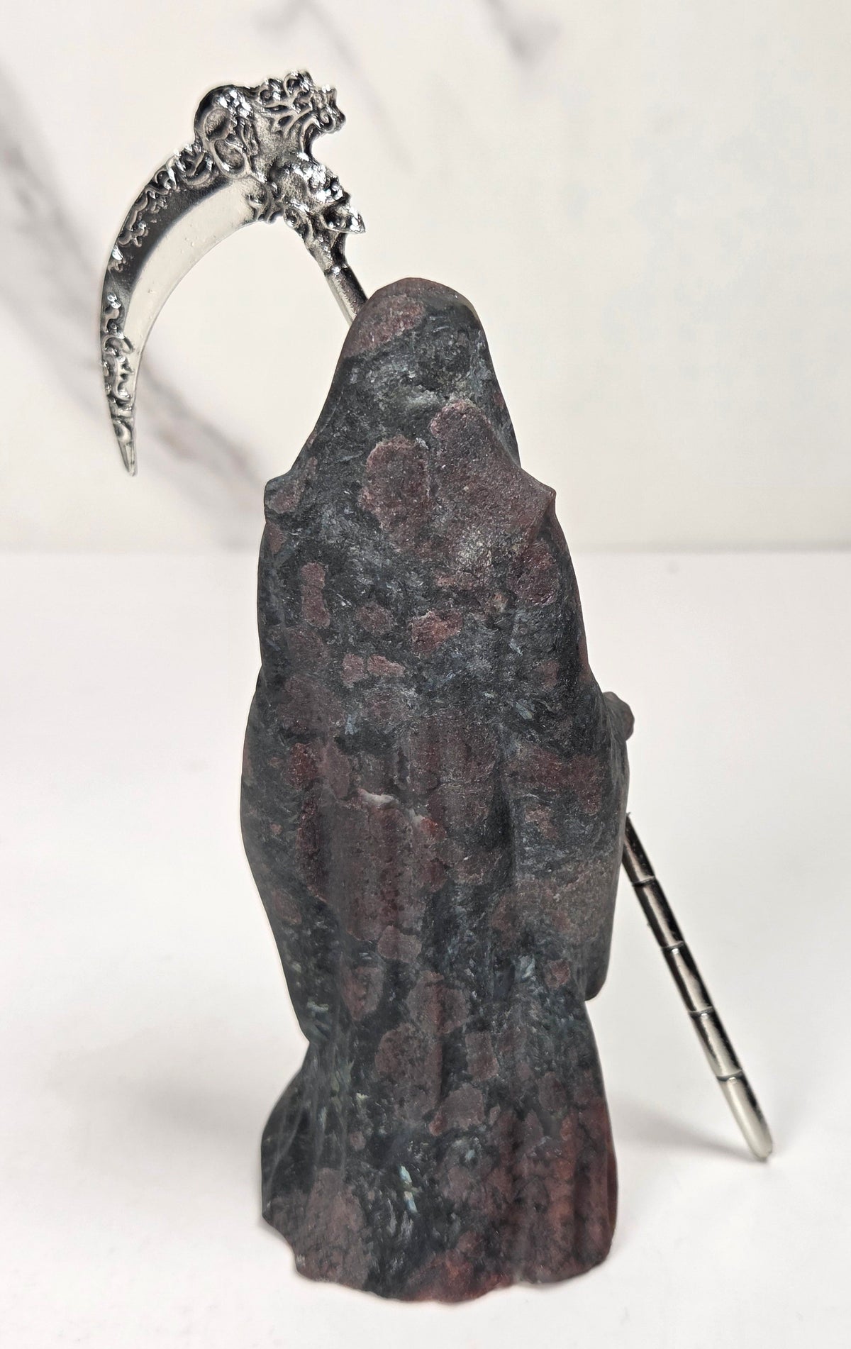 Reaper style crystal carving with black and red coloring with a metal scythe against a marbled background