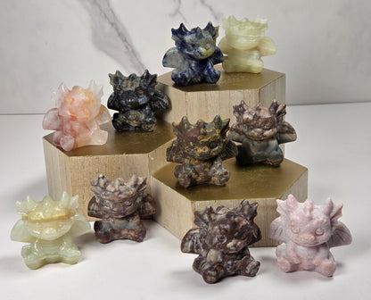 A collection of small crystal dragon figurines in varying colors on a wood stand against a white background