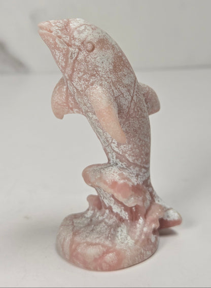 Dolphins on wave carving made of pink opal against a marbled background