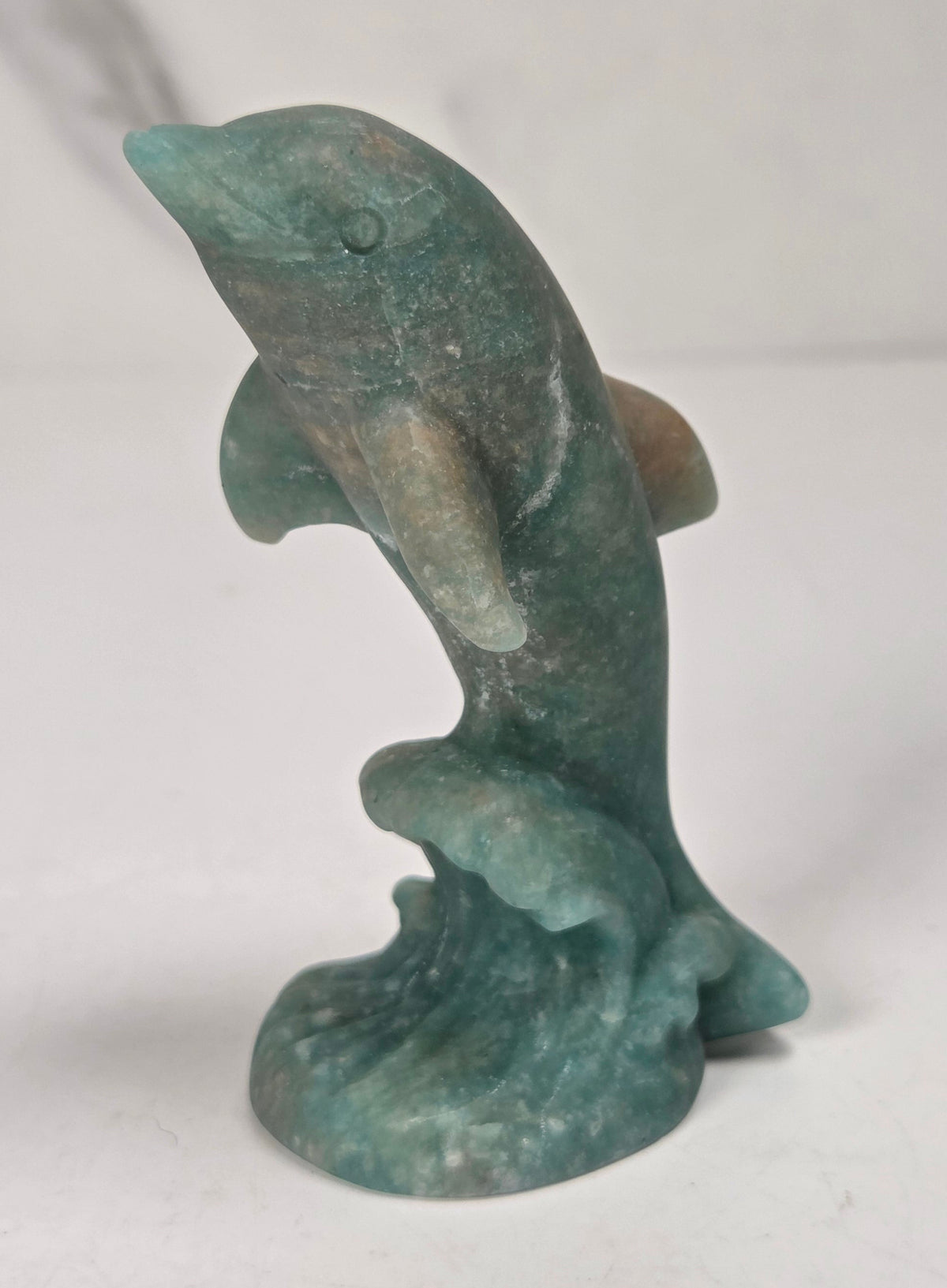 Dolphin on wave carving made of amazonite mineral against a marbled background