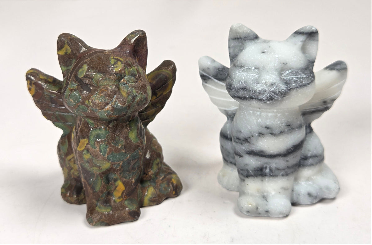 Crystal cat carvings with wings in a variety of colors and materials against a marbled background