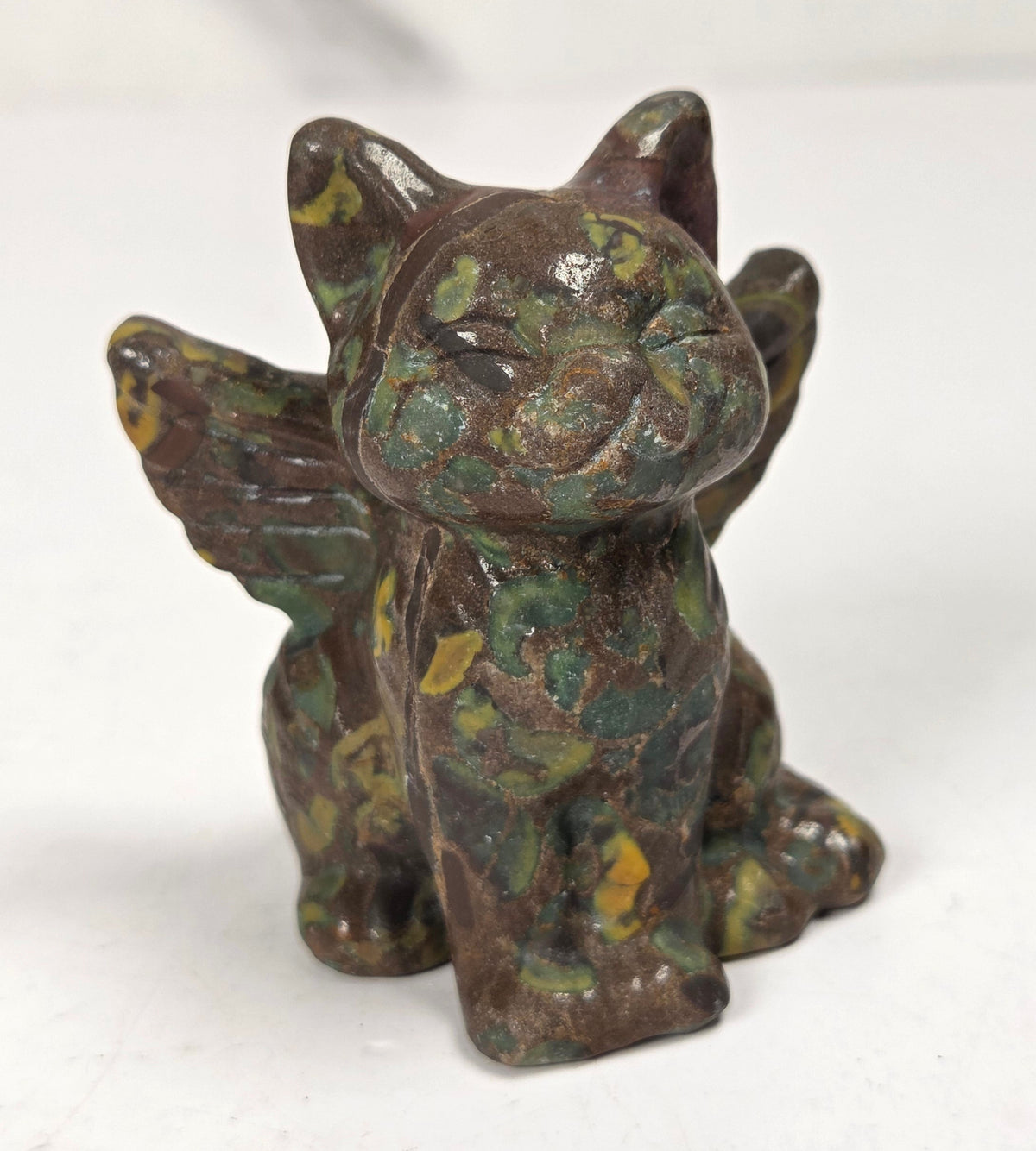 Crystal cat carving with wings made of a tan, green and yellow mineral against a marbled background