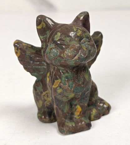Crystal cat carving with wings made of a tan, green and yellow mineral against a marbled background