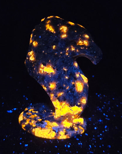 Crystal eagle head carving made of yooperlite glowing orange under a UV light against a dark background