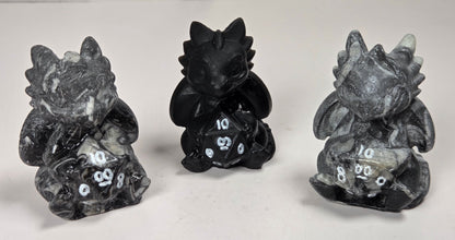 Set of 3 dragon-like carvings holding a multi-faceted die set against a white background