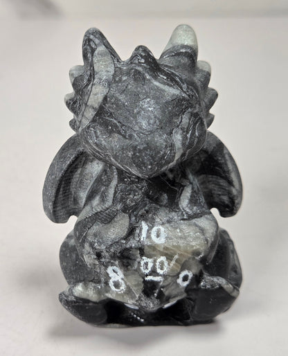 Black and grey marbled dragon-like crystal carving holding a multi-faceted die set against a white background