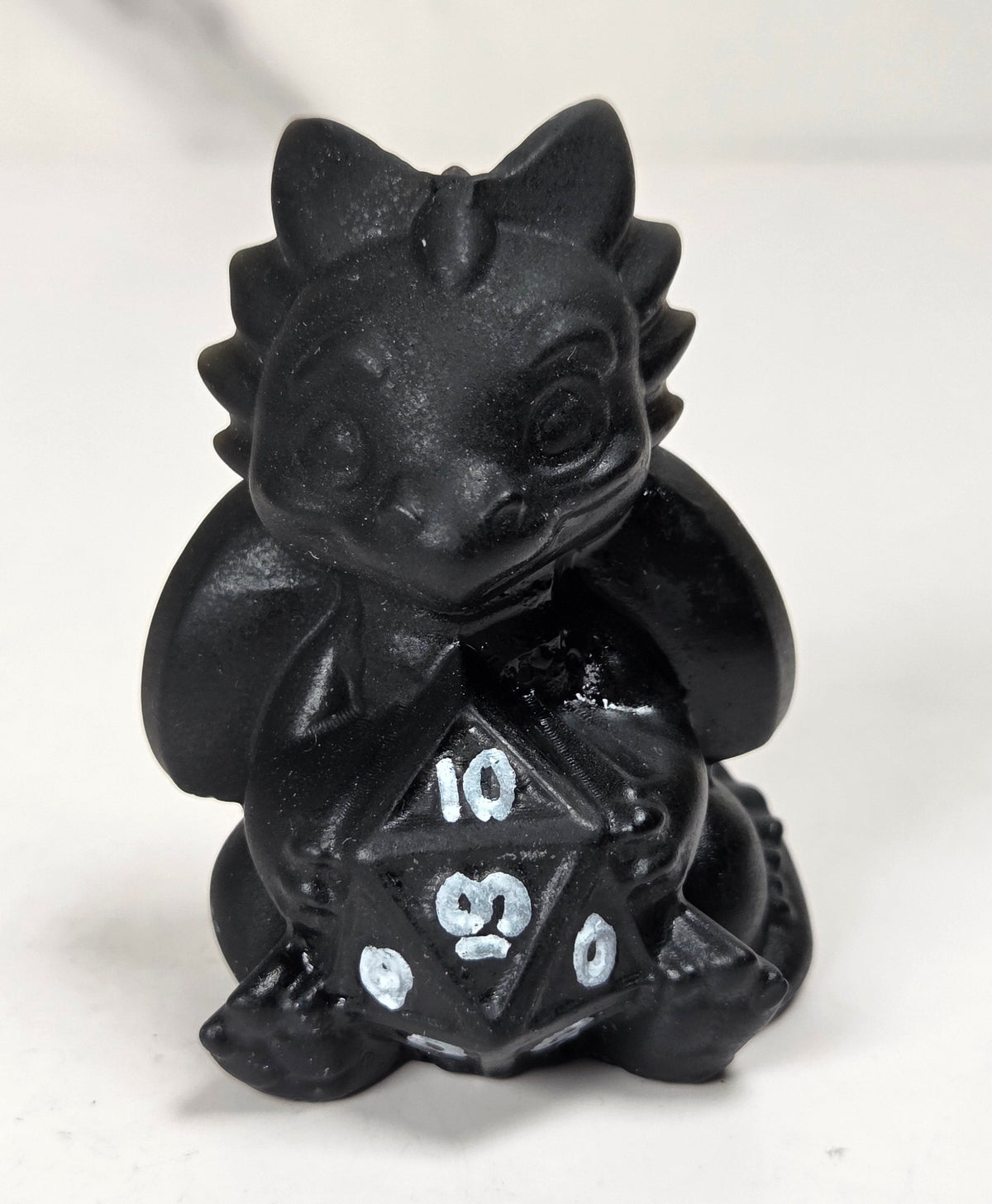 Black dragon-like crystal carving holding a multi-faceted die set against a white background