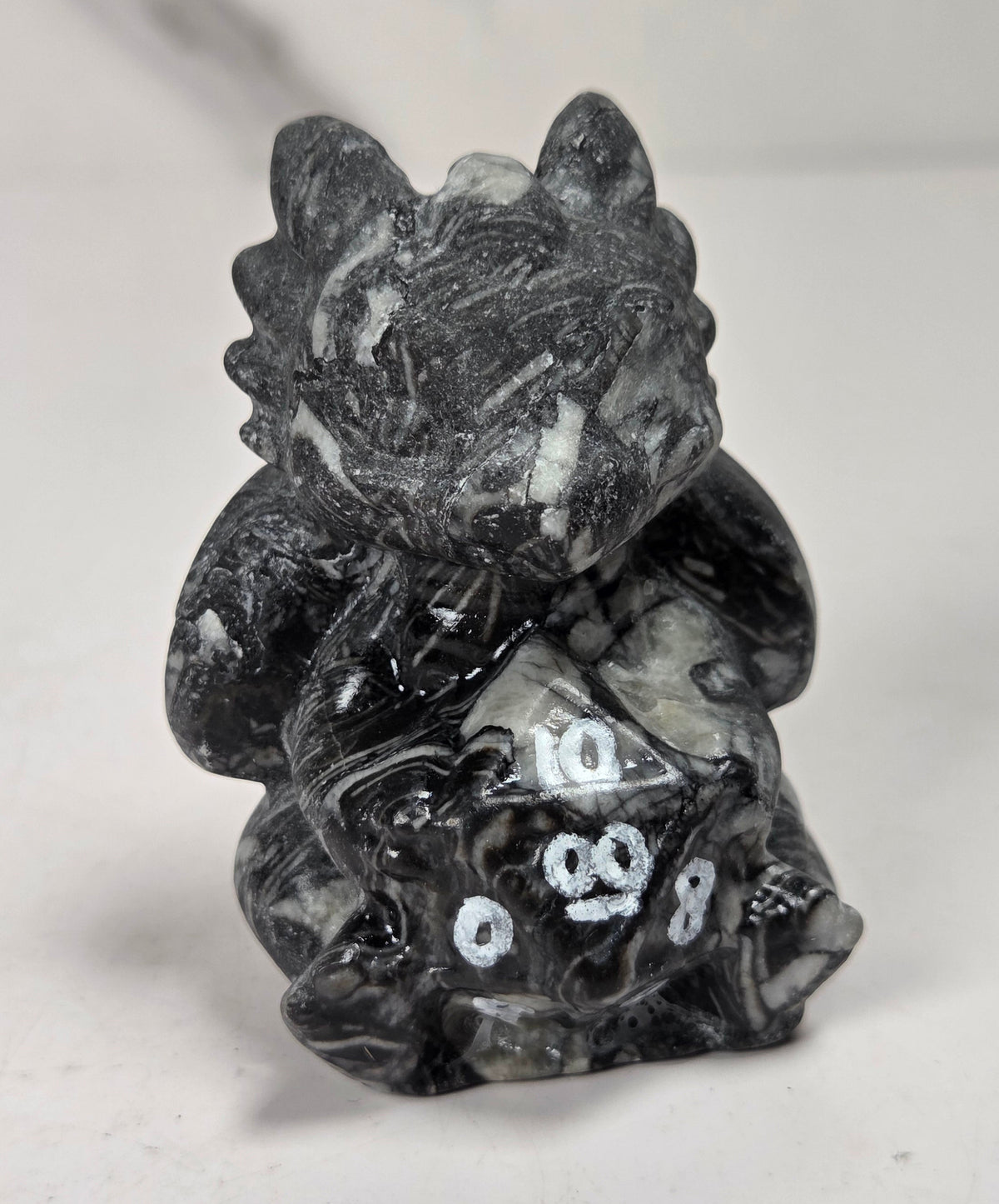 Black and grey marbled dragon-like crystal carving holding a multi-faceted die set against a white background