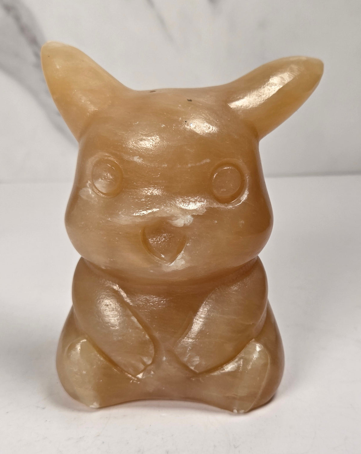 Orange calcite Pikachu style carving against a marbled background