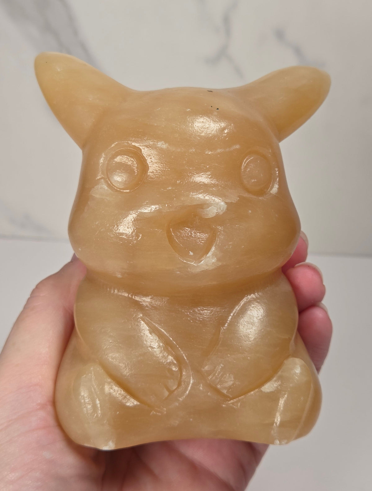 Hand holding an Orange calcite Pikachu style carving against a marbled background