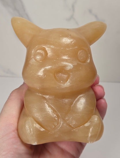 Hand holding an Orange calcite Pikachu style carving against a marbled background