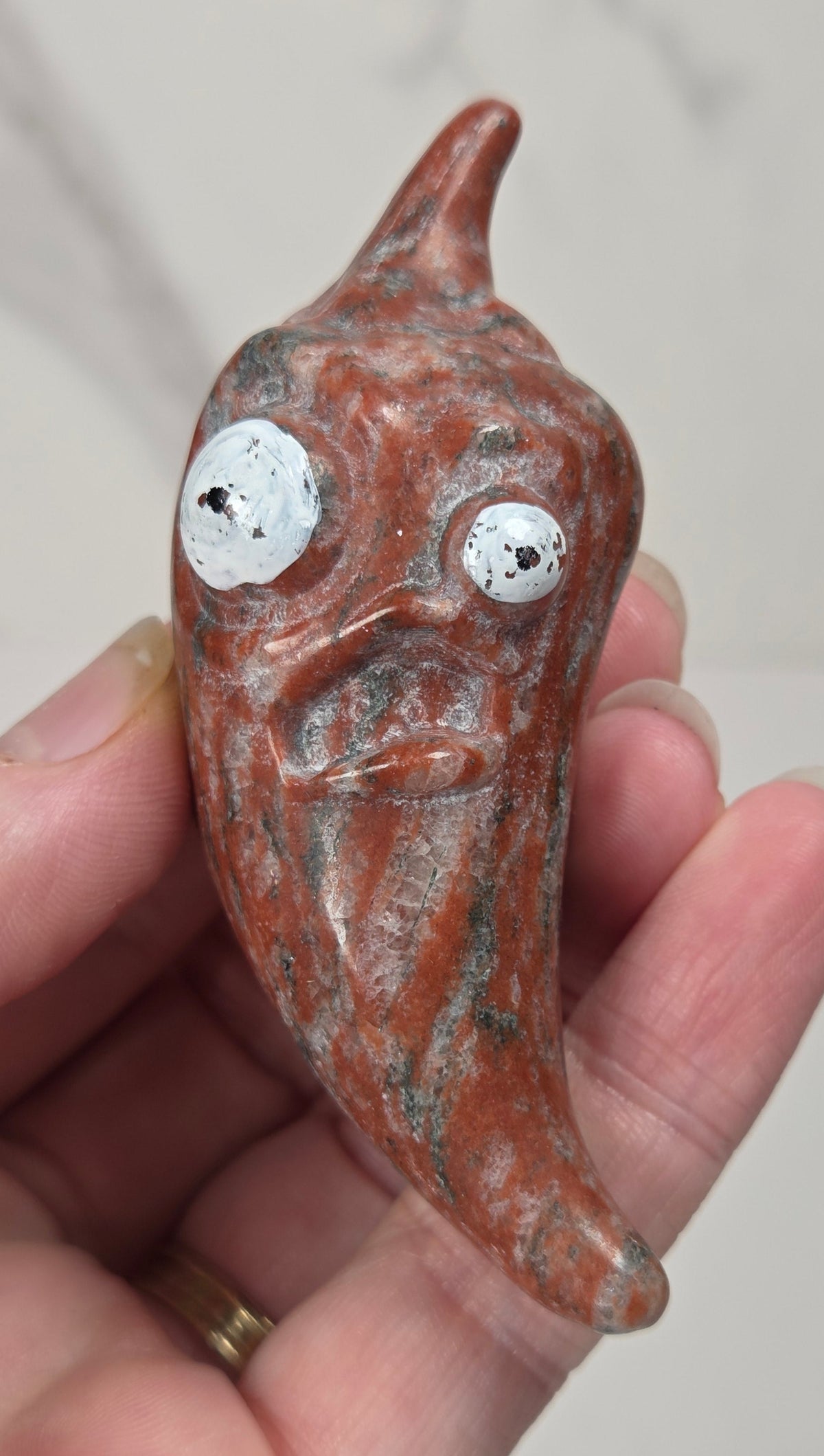 Hand holding a red and black crystal pepper carving with two sized eyes against a white background