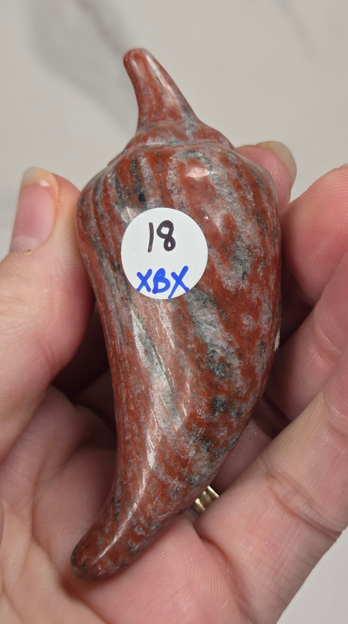 Hand holding a red and black crystal pepper carving against a white background