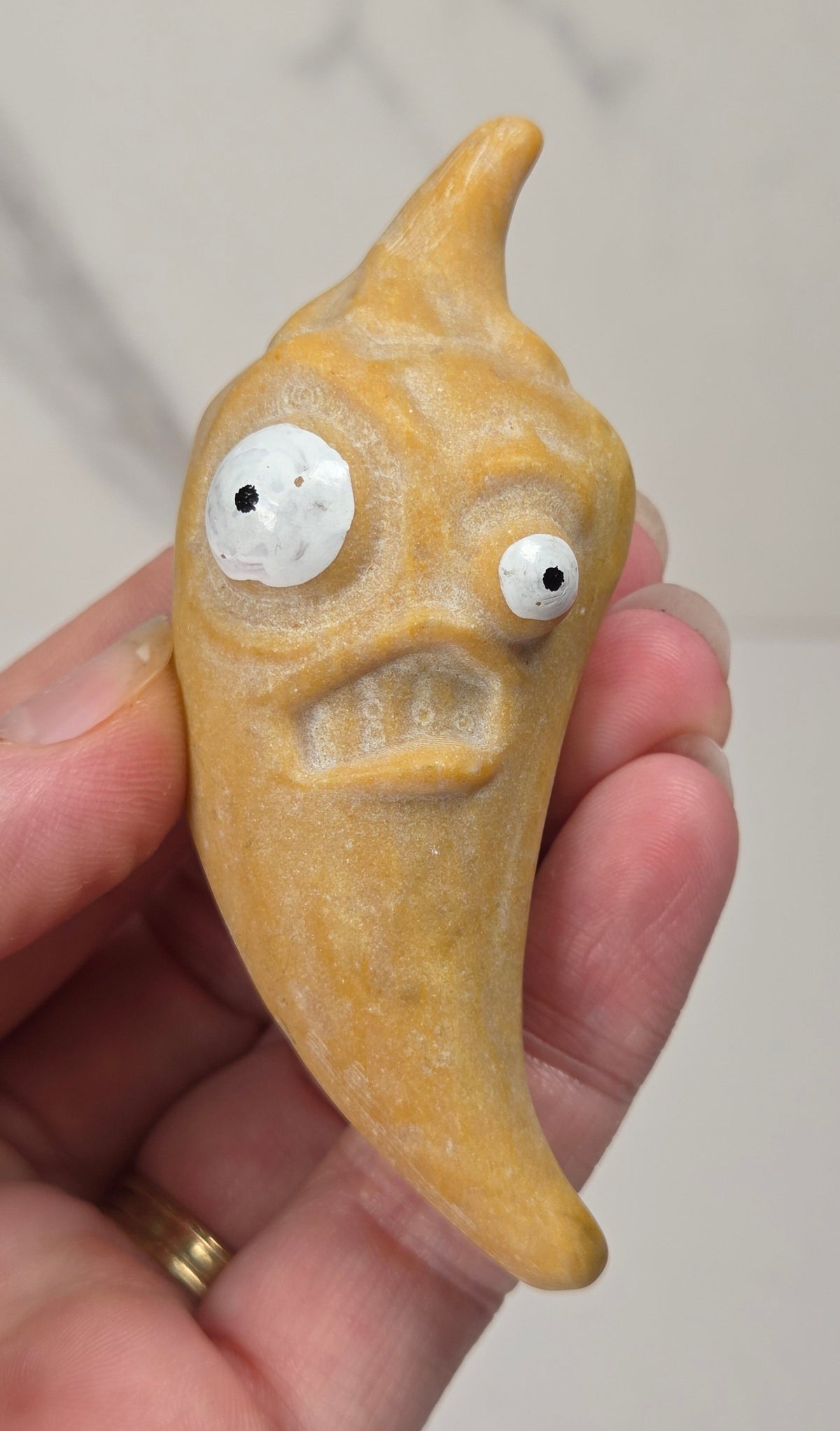 Hand holding a yellow crystal pepper carving with two sized eyes against a white background
