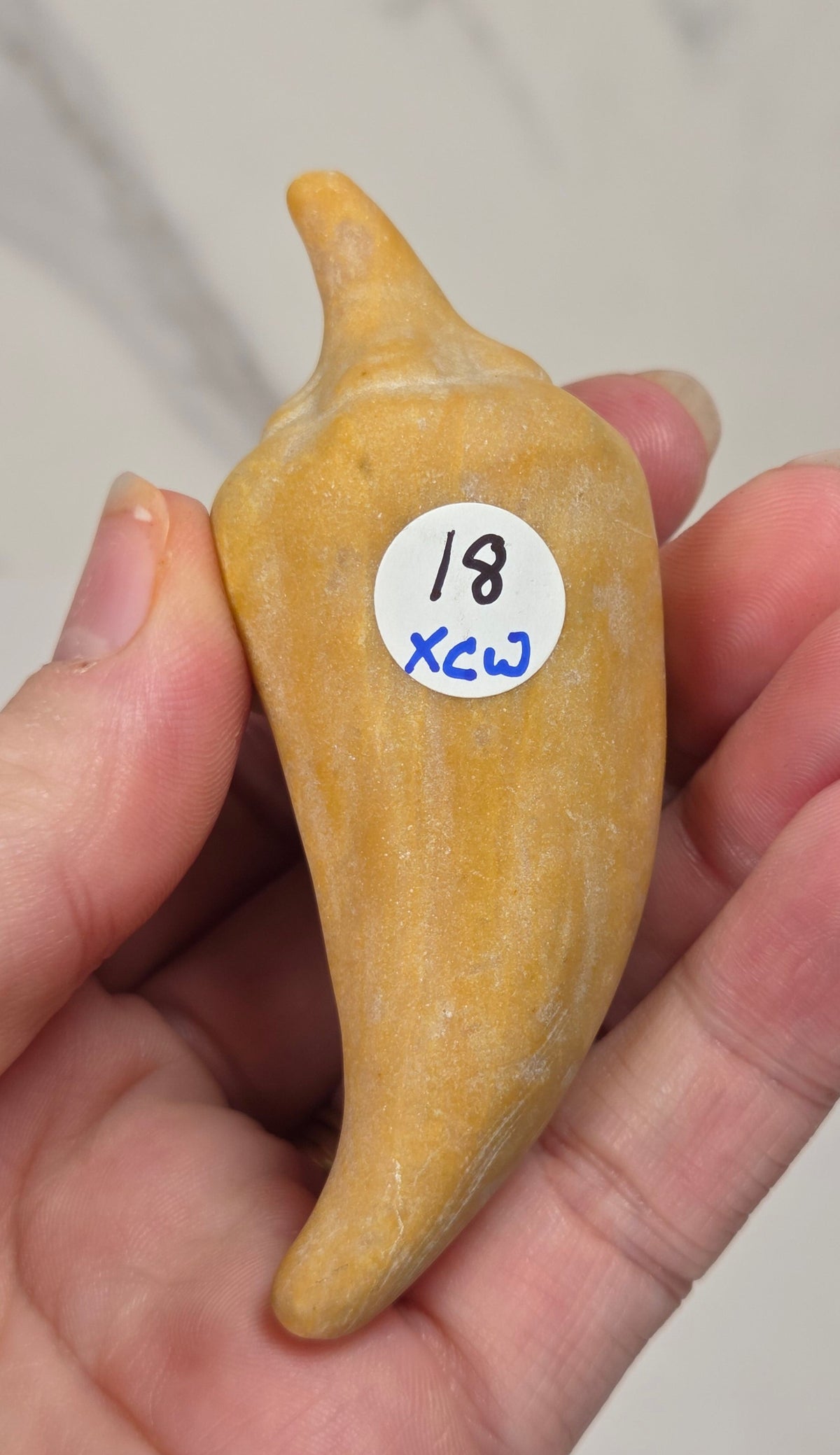 Hand holding a yellow crystal pepper carving against a white background