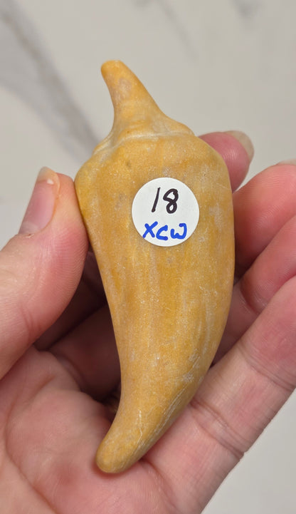 Hand holding a yellow crystal pepper carving against a white background