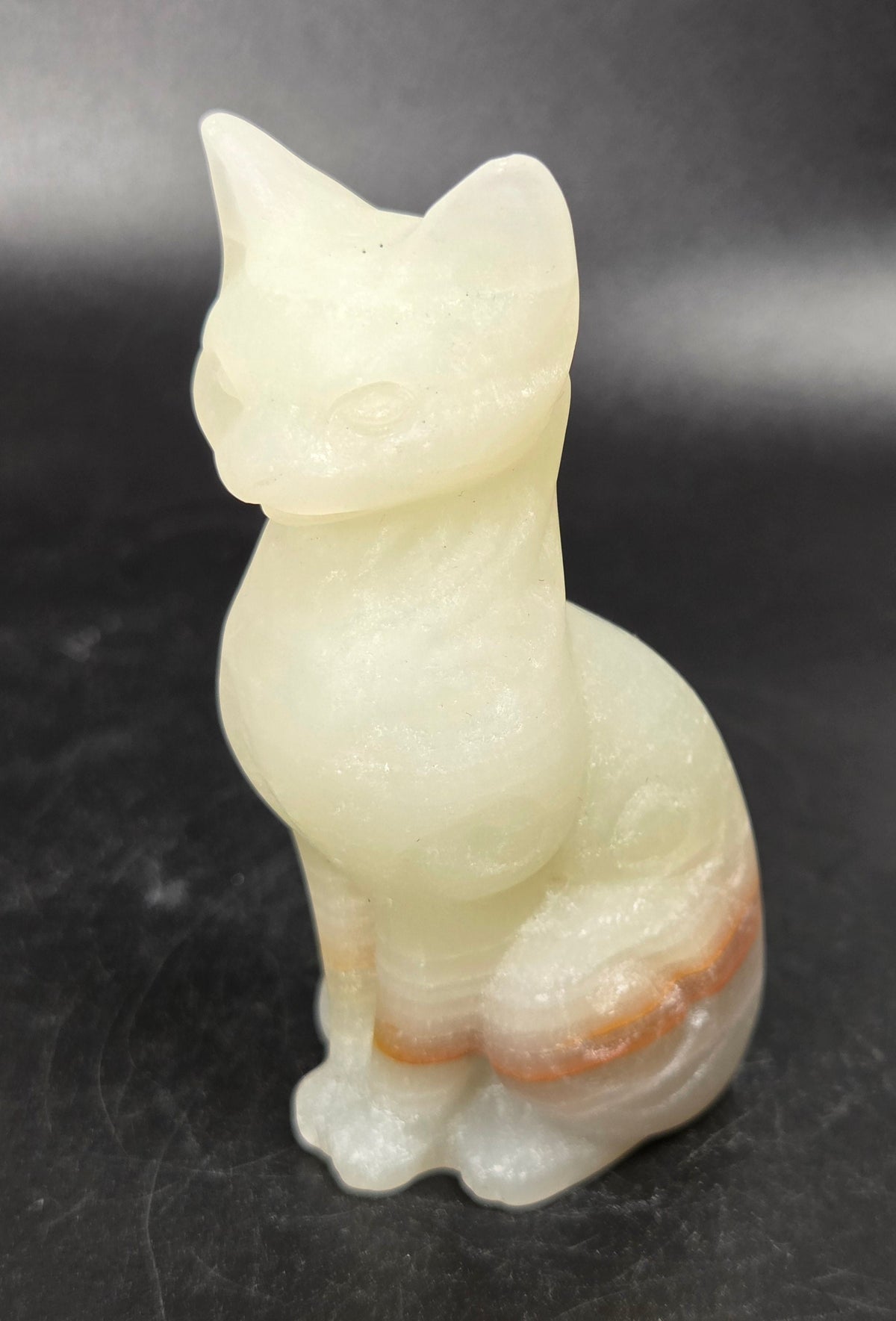 Yellowish crystal cat shaped carving with scroll work against a black background