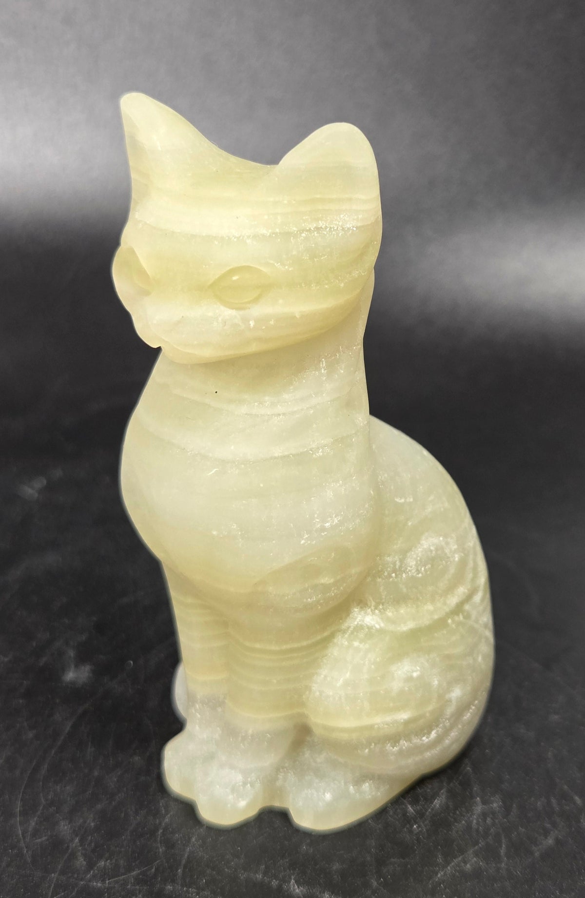 Yellowish crystal cat shaped carving with scroll work against a black background