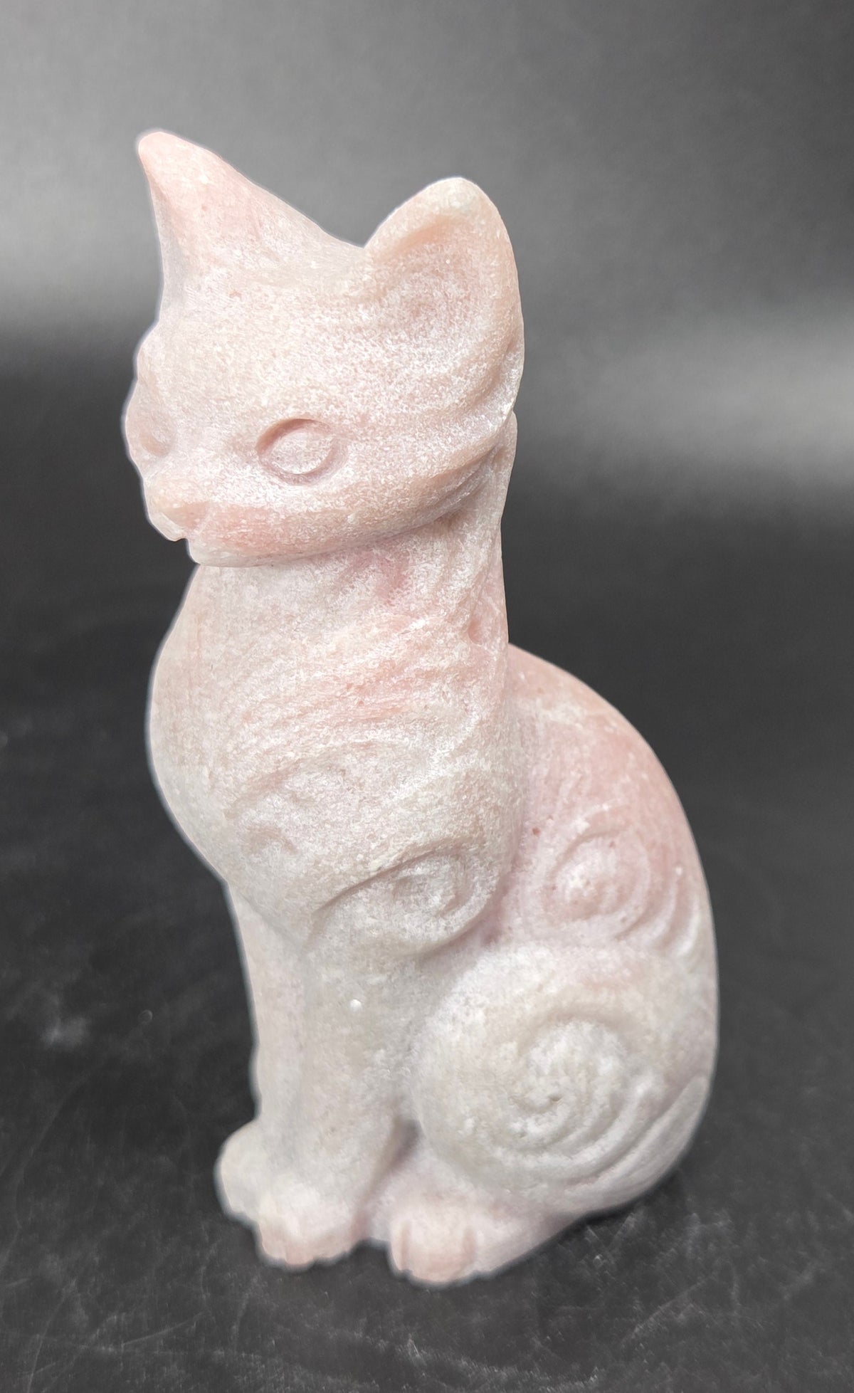 Pink crystal cat shaped carving with scroll work against a black background