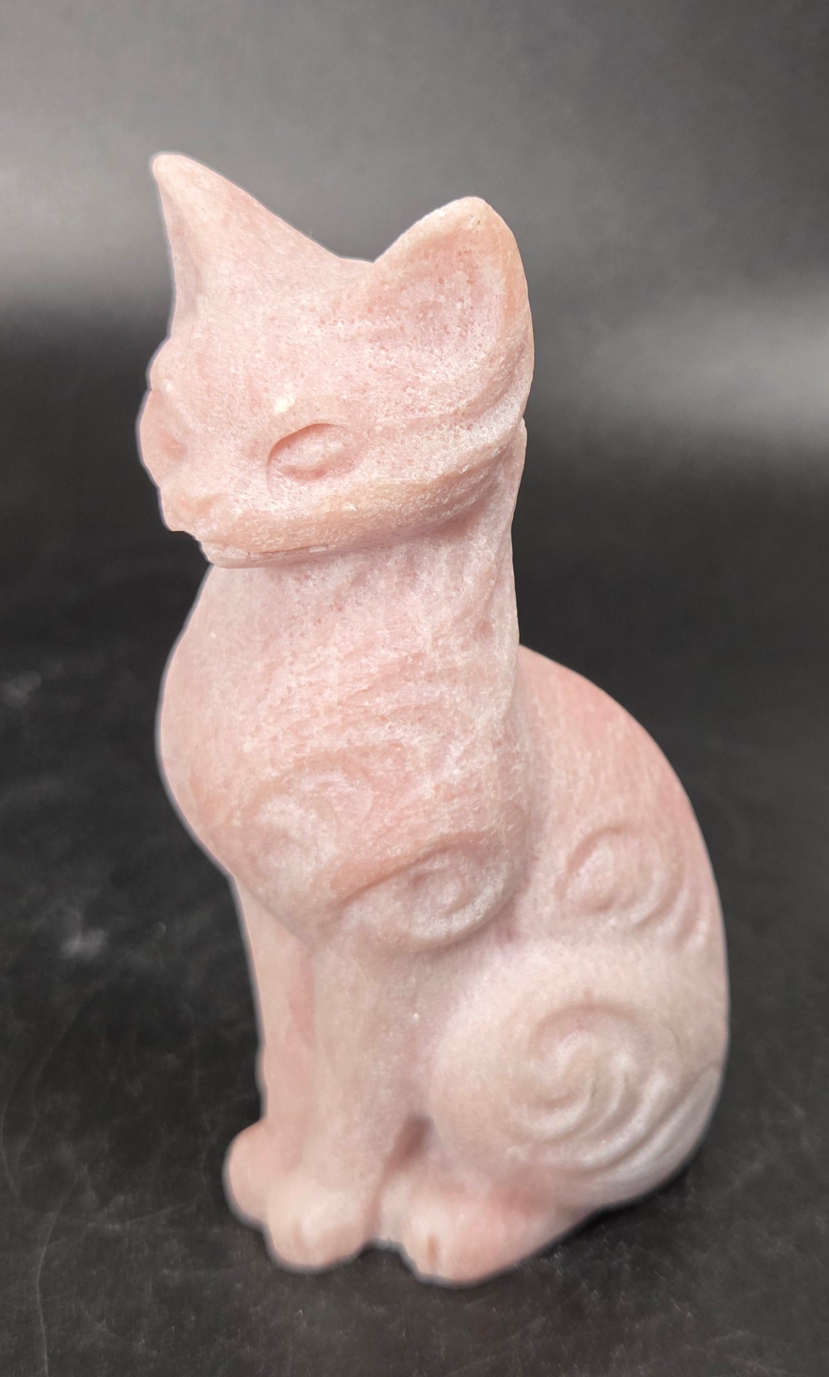 Pink crystal cat shaped carving with scroll work against a black background